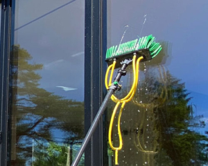Grønt rengjøringsverktøy med gul slange vasker vinduer på et bygg