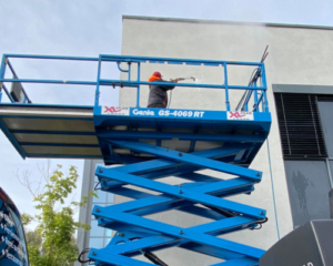 Mann i blå arbeidsklær vasker vinduer på en høy bygning fra en heisplattform